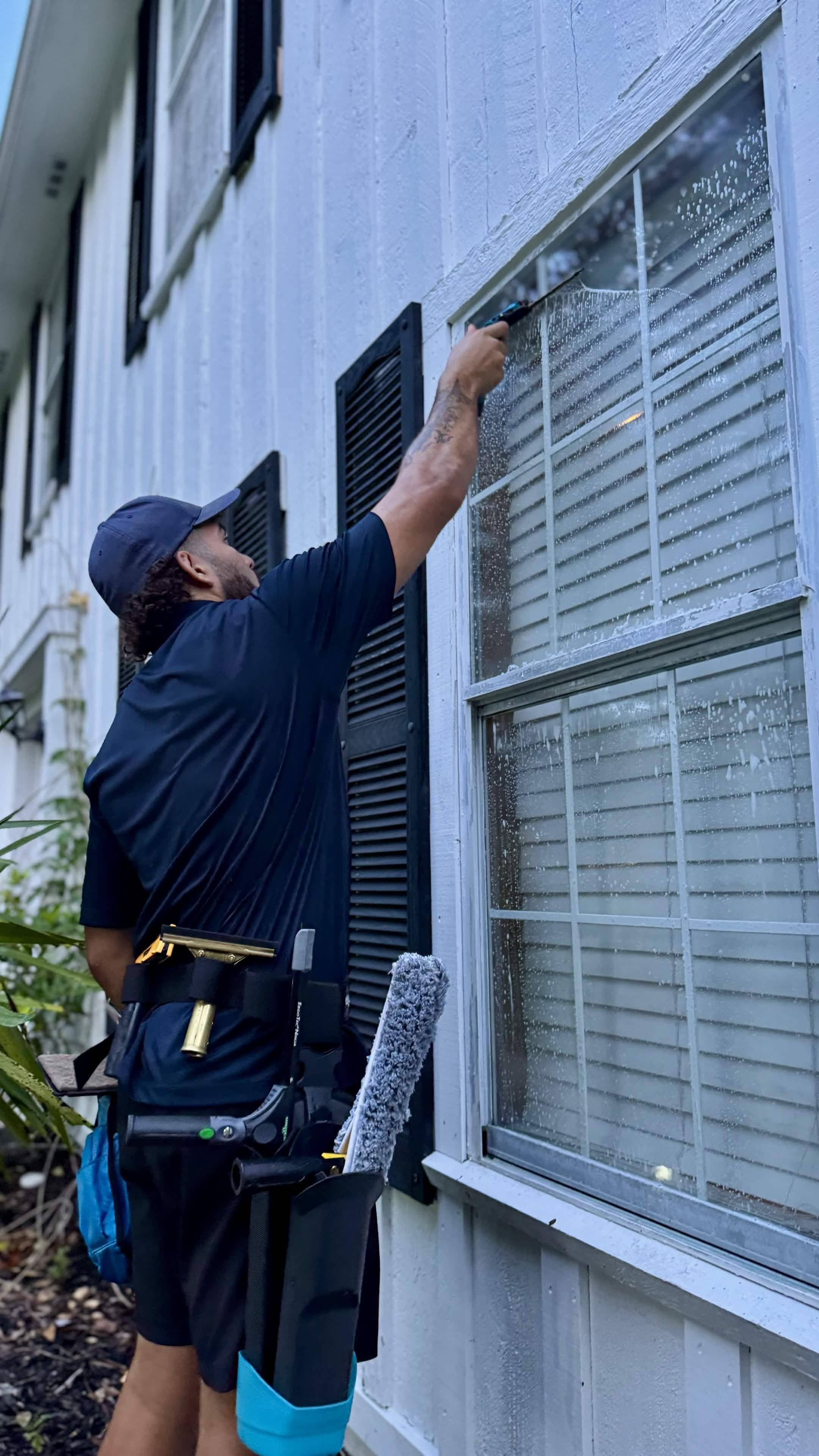 CrestFlow technician reaching up to squeegee an exterior window on a white clapboard house